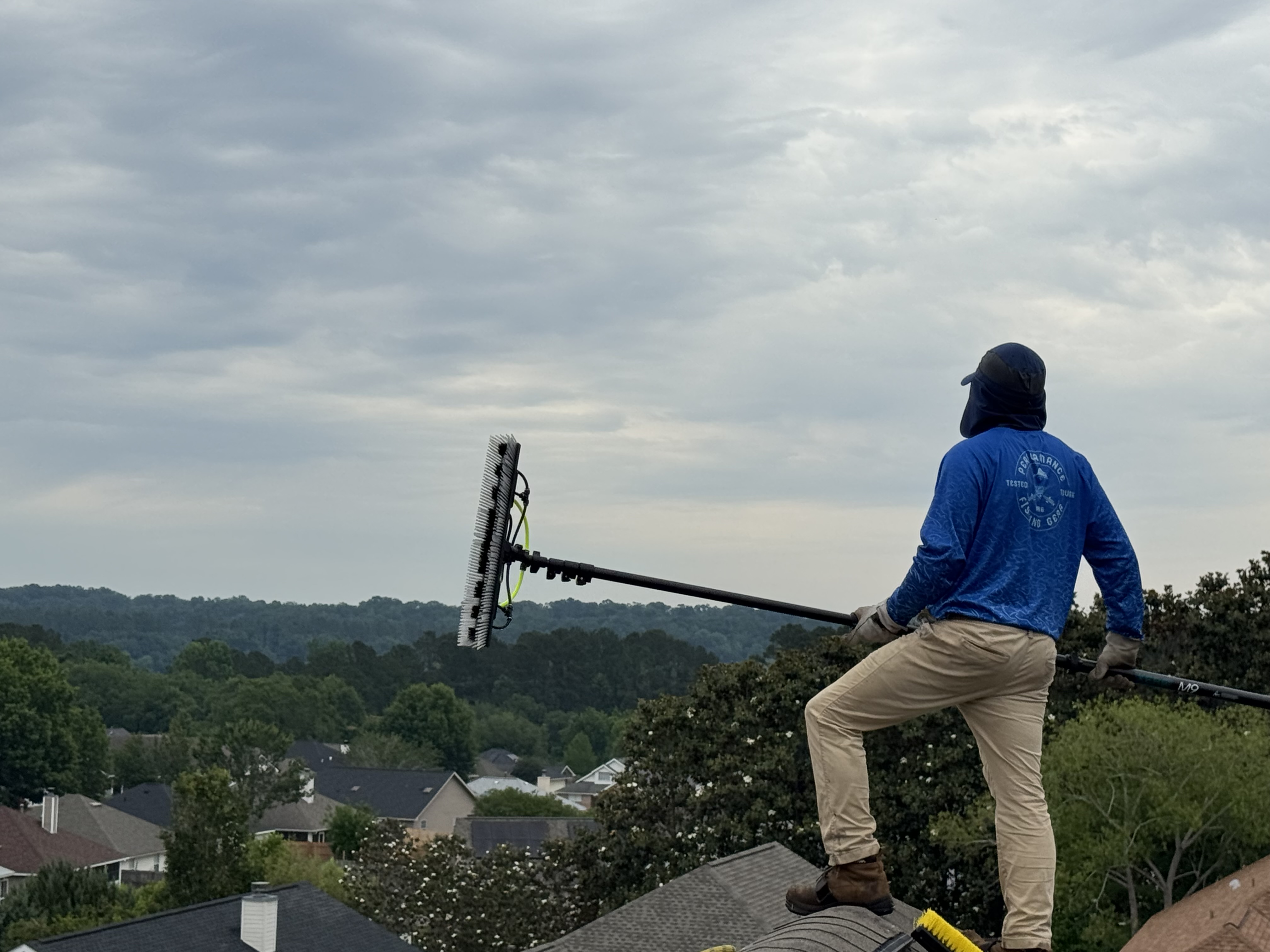 Genesis Solar Systems technician on a roof with a solar panel cleaning brush overlooking a neighborhood